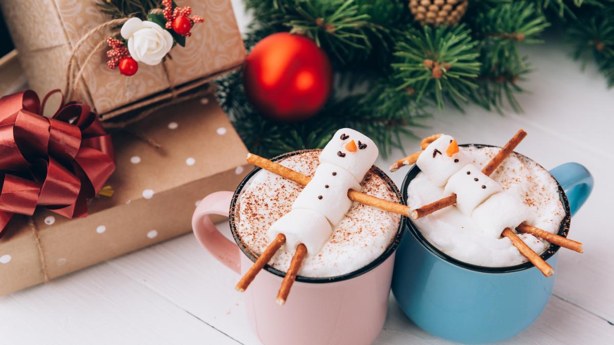 Two mugs of hot chocolate with marshmallow snowmen on top.