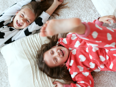 Two children laying on the floor with their pajamas on.