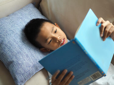 Boy laying on a couch reading a book