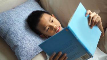 Boy laying on a couch reading a book