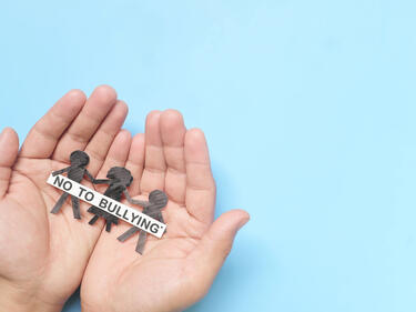 Two hands holding a paper cutout of three people and the sign "no to bullying"