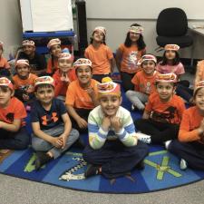 Students sitting on a carpet wearing orange shirts.