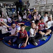 Students sitting on a carpet holding cereal bowls.