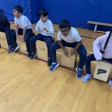 Students sitting on box drums in a gym.