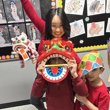 A teacher and a student wearing red with a paper dragon.