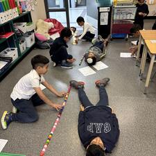 Students measuring another student using cubes