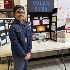 Student in front of a science fair project wearing a medal