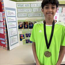Student in front of a science fair project wearing a medal