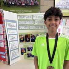 Student in front of a science fair project wearing a medal