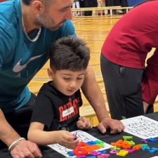 A young boy doing a puzzle with his dad.